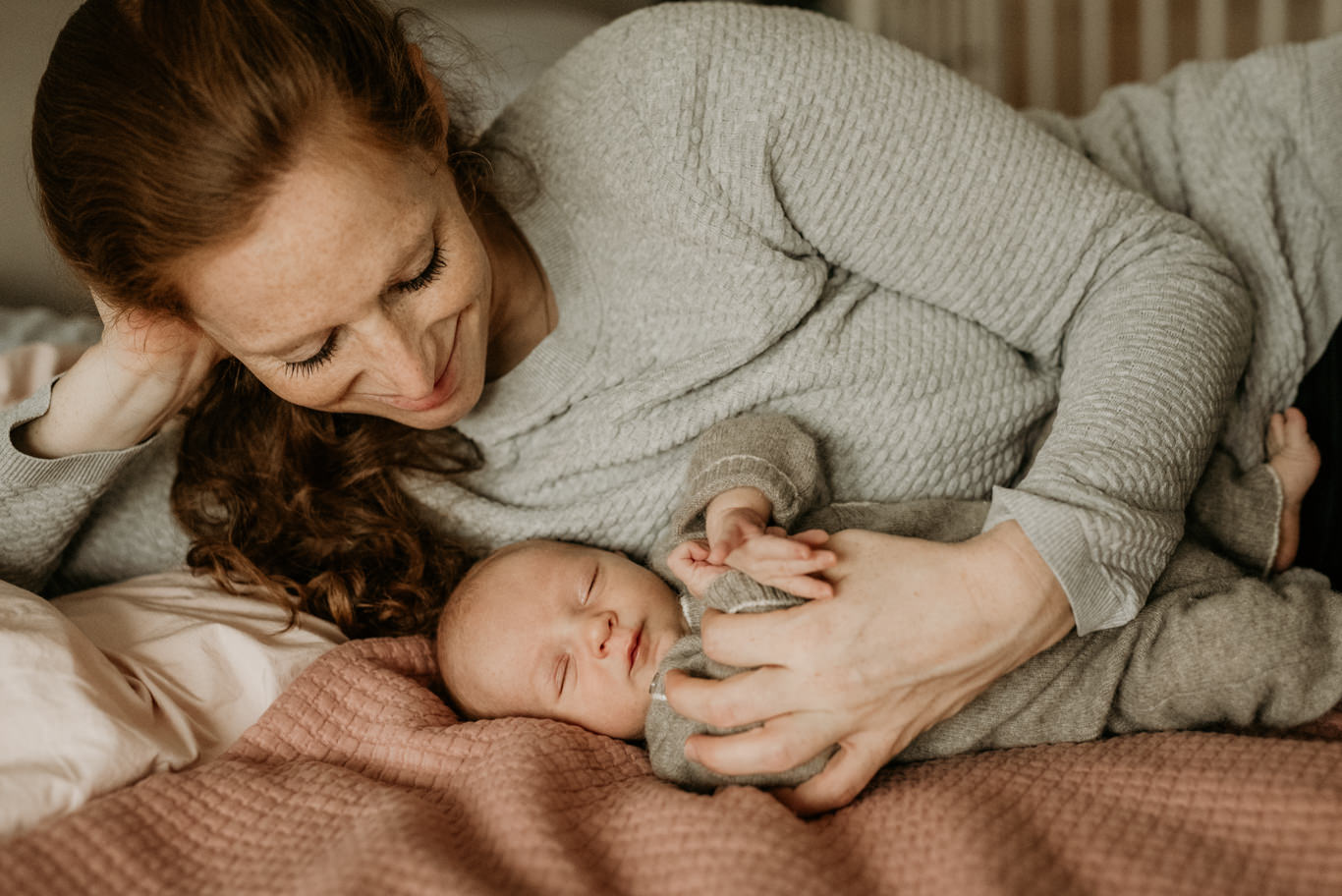 Mutter kuschelt lächelnd mit ihrem schlafenden Neugeborenen im Bett