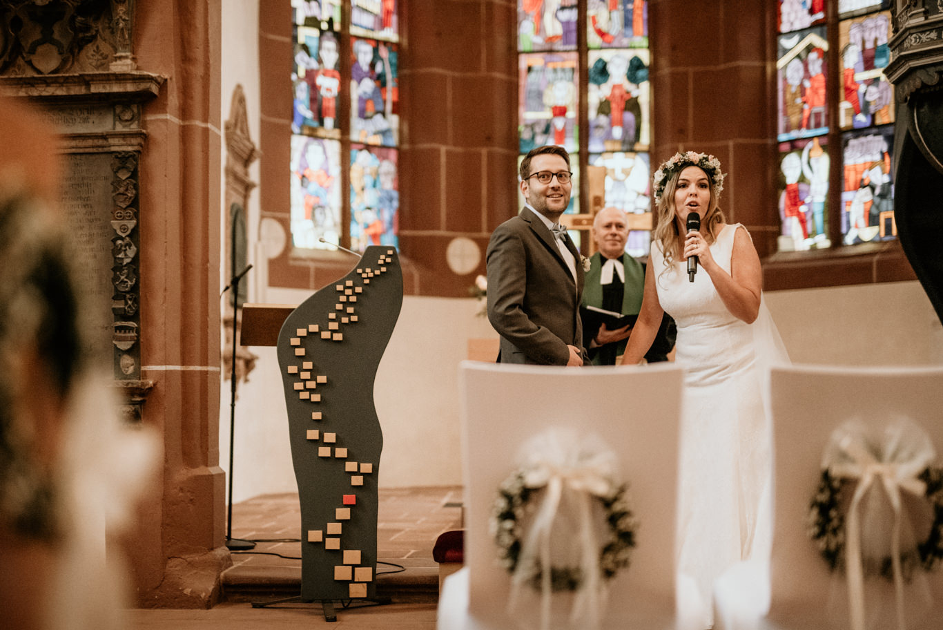Bräutigam hält Mikrofon neben lachender Braut am Altar