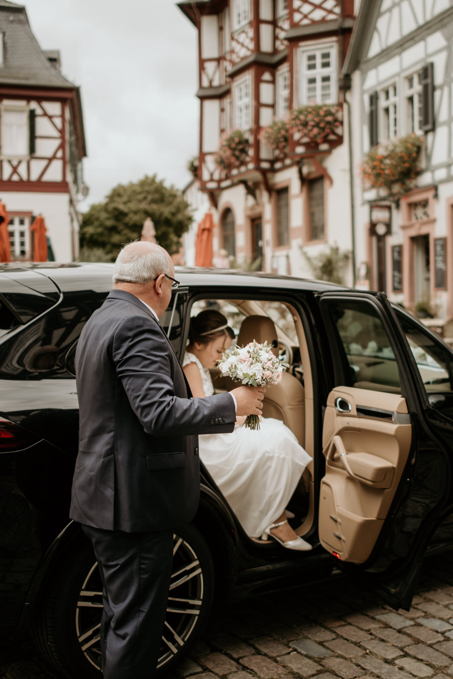 Brautvater hilft Braut beim Aussteigen aus dem Hochzeitsauto