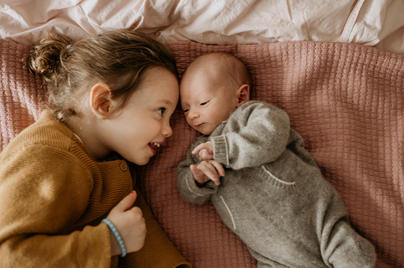 Kleine Schwester liegt lachend neben ihrem neugeborenen Geschwisterchen