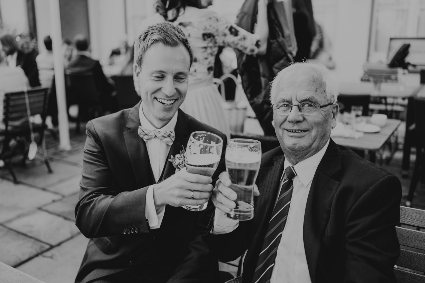 Bräutigam stößt mit älterem Gast auf Bier an, Schwarzweißaufnahme