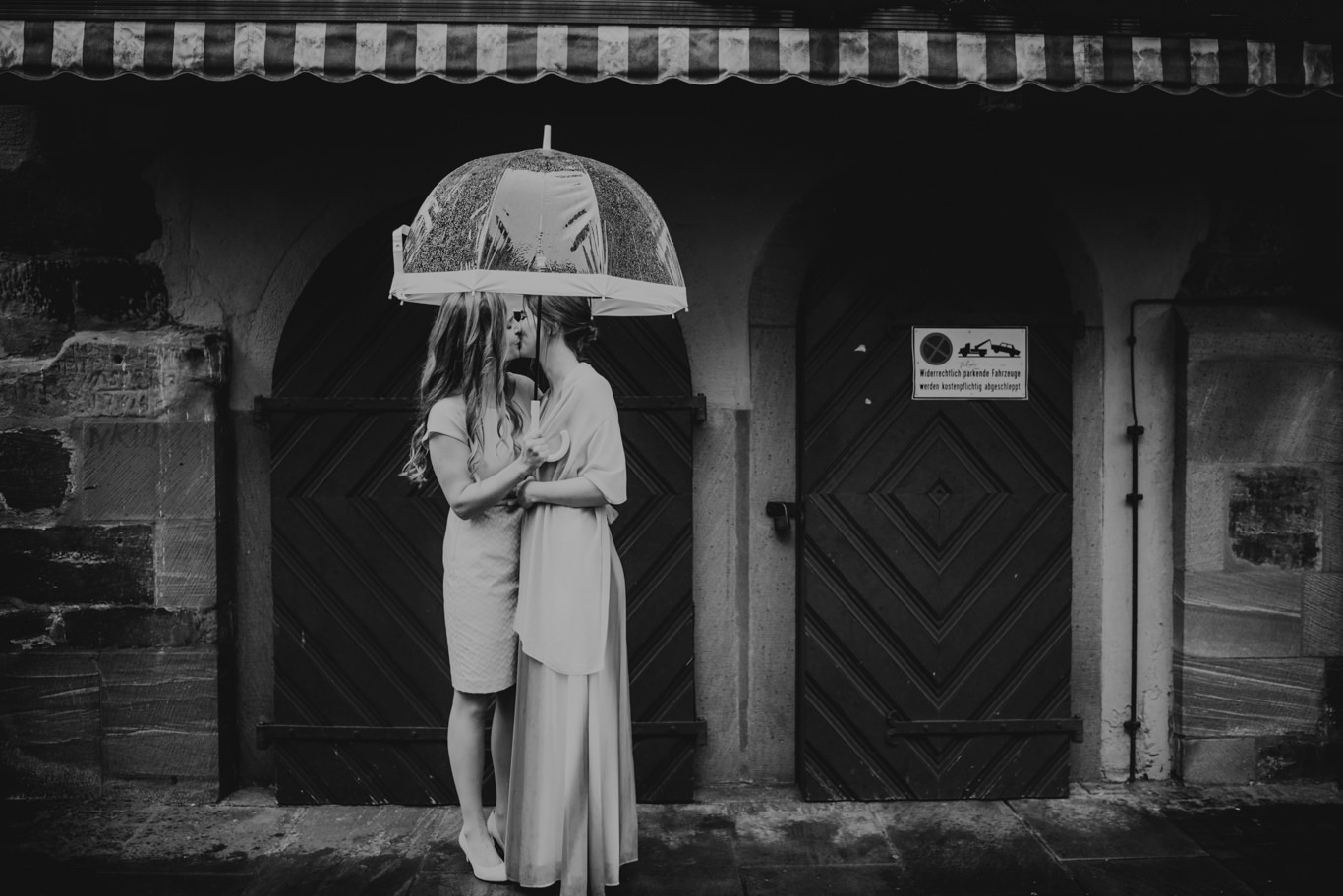 Schwarzweißaufnahme zweier Frauen unter Regenschirm vor historischer Tür