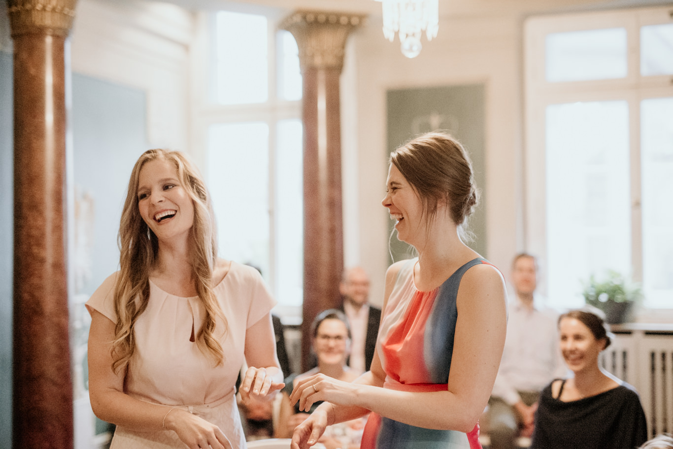 Zwei Bräute lachen sich an, im Hintergrund applaudierende Gäste
