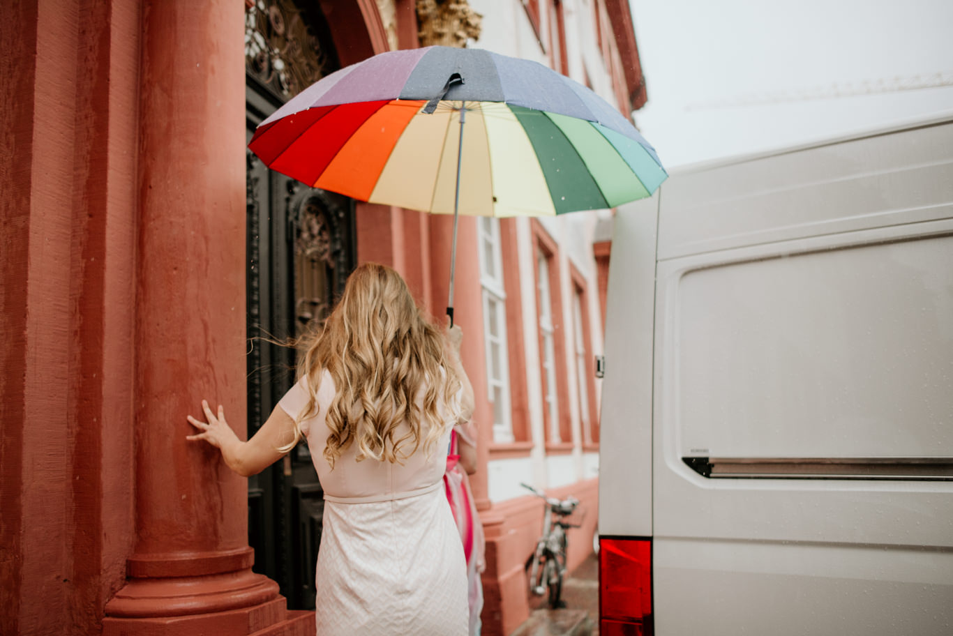 Frau hält bunten Regenschirm vor rotem Sandsteingebäude