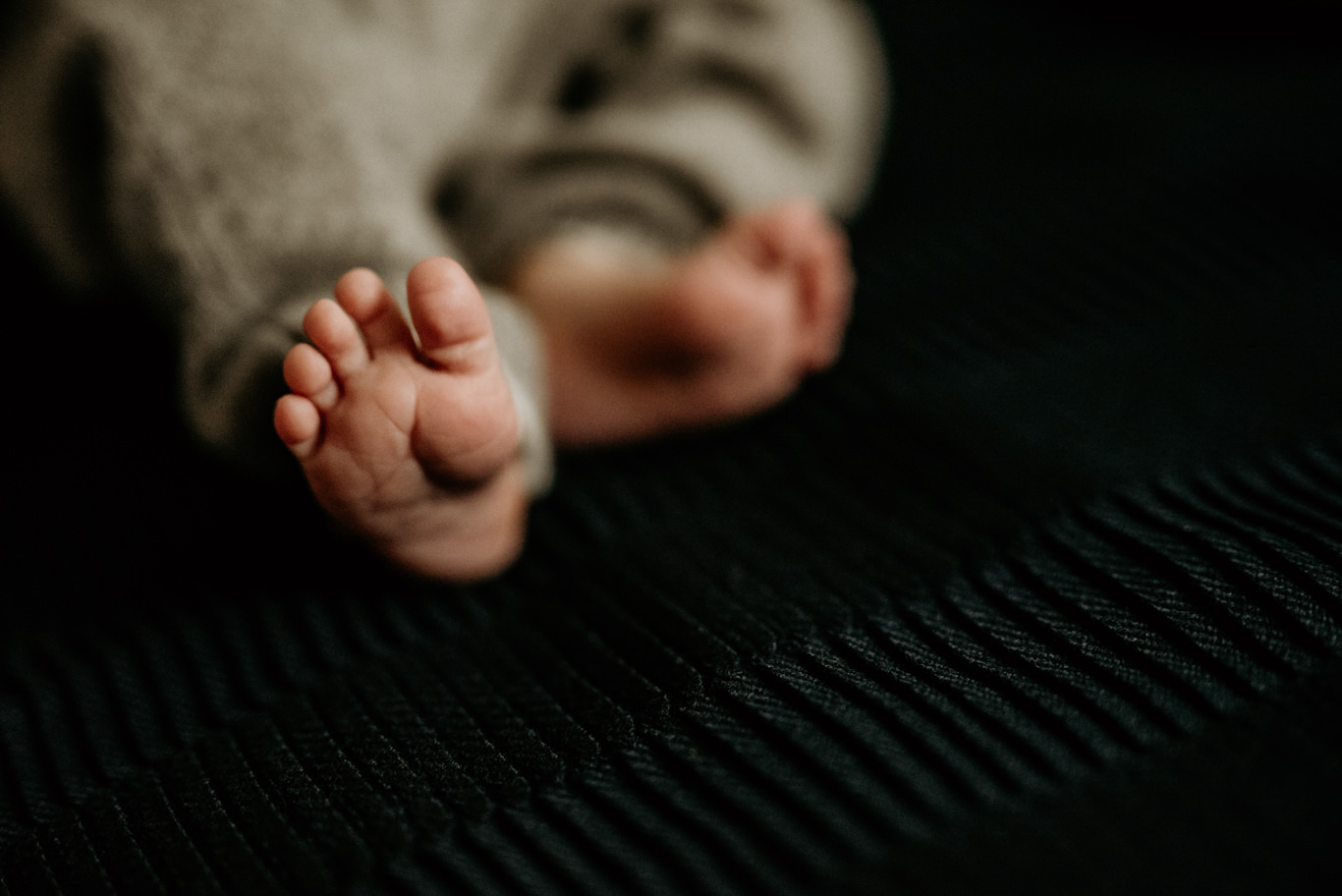 Nahaufnahme von Babyfüßen und Kopf auf dunkler Decke