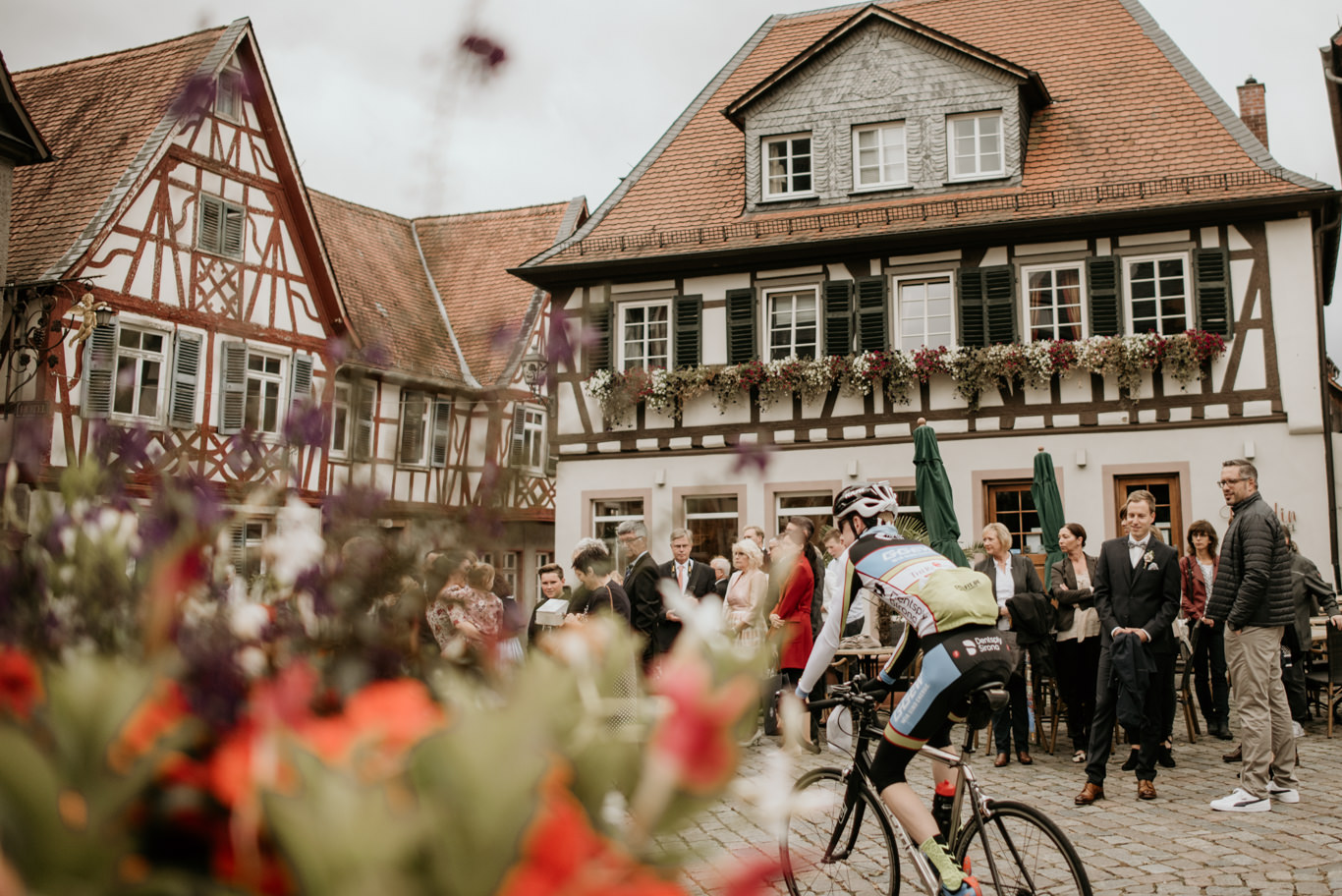Hochzeitsgäste stehen am Marktplatz, während ein Radfahrer vorbeifährt