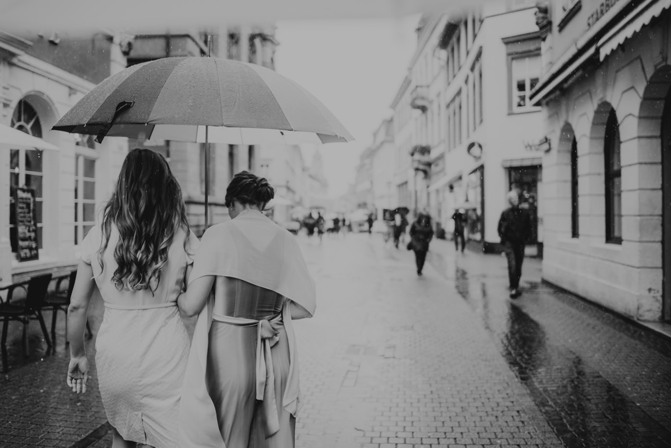 Schwarzweißaufnahme zweier Frauen, die durch regennasse Gasse gehen