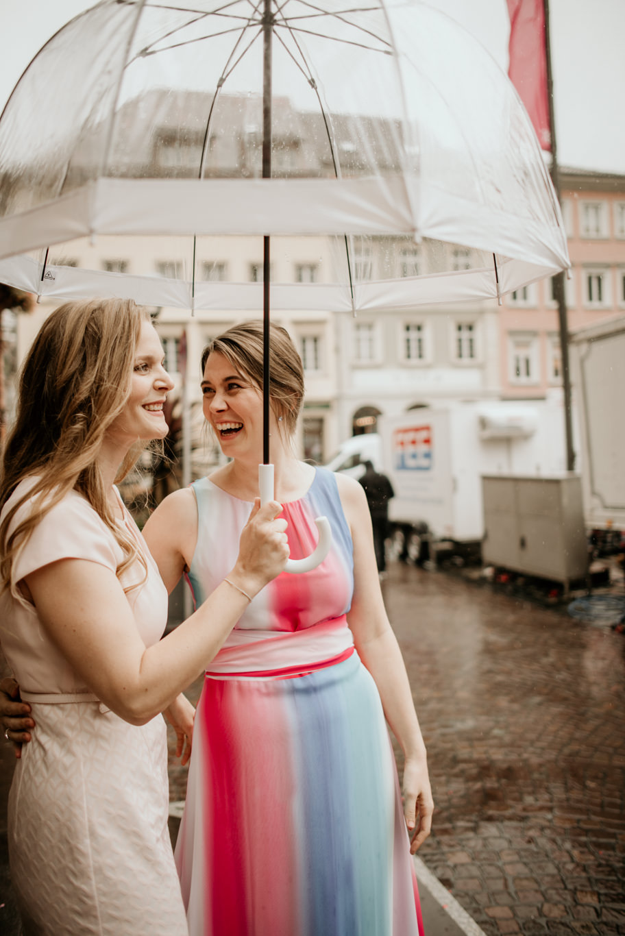 Zwei Frauen lachen unter einem durchsichtigen Regenschirm in der Altstadt
