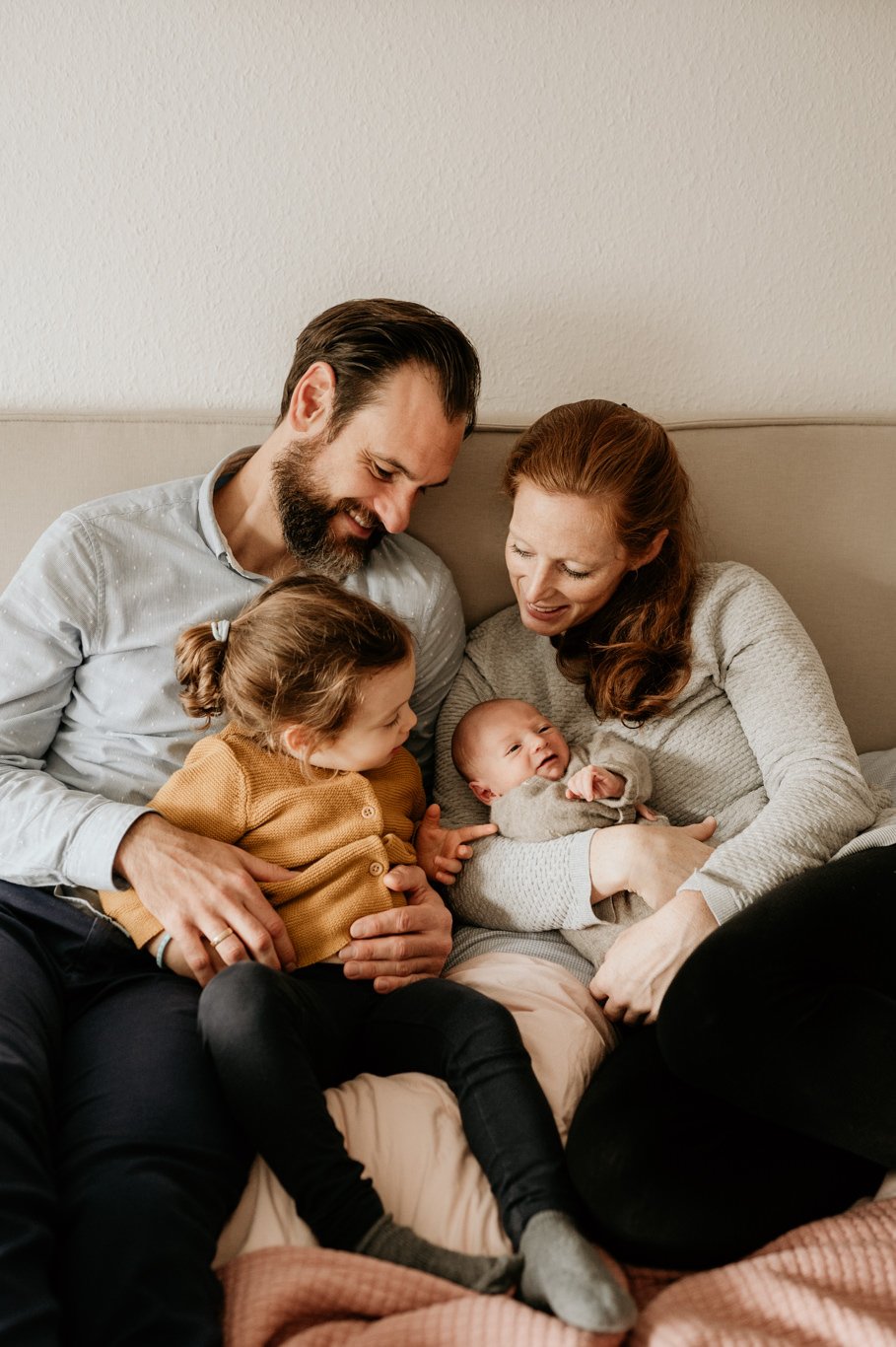 Eltern sitzen mit Kleinkind und Baby zusammen auf dem Sofa