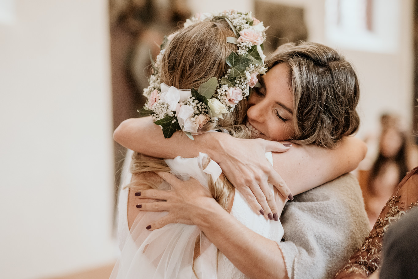 Braut mit Blumenkranz umarmt eine lächelnde Gästin