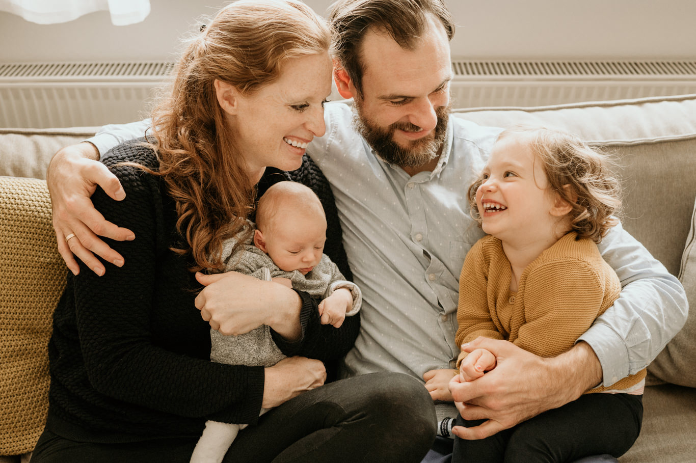 Eltern sitzen lachend mit Baby und Tochter auf dem Sofa
