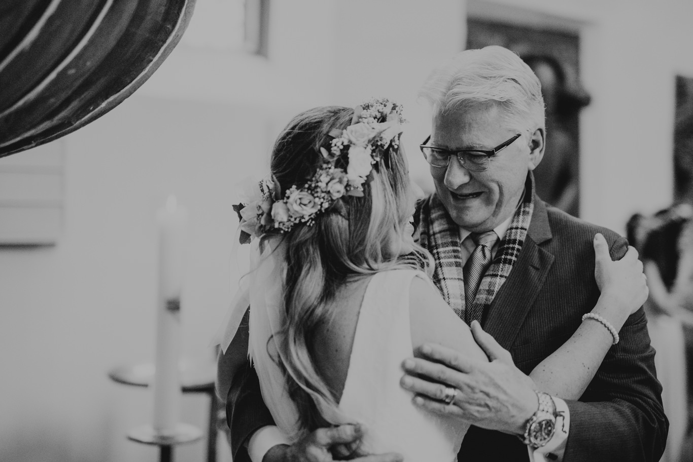 Braut mit Blumenkranz umarmt einen älteren Gast, Schwarzweißaufnahme