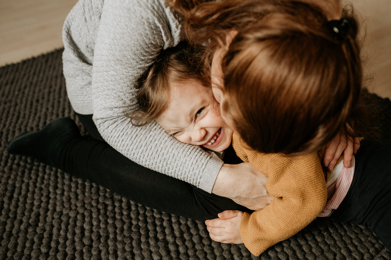 Kleinkind umarmt lachend seine Schwester auf der Decke