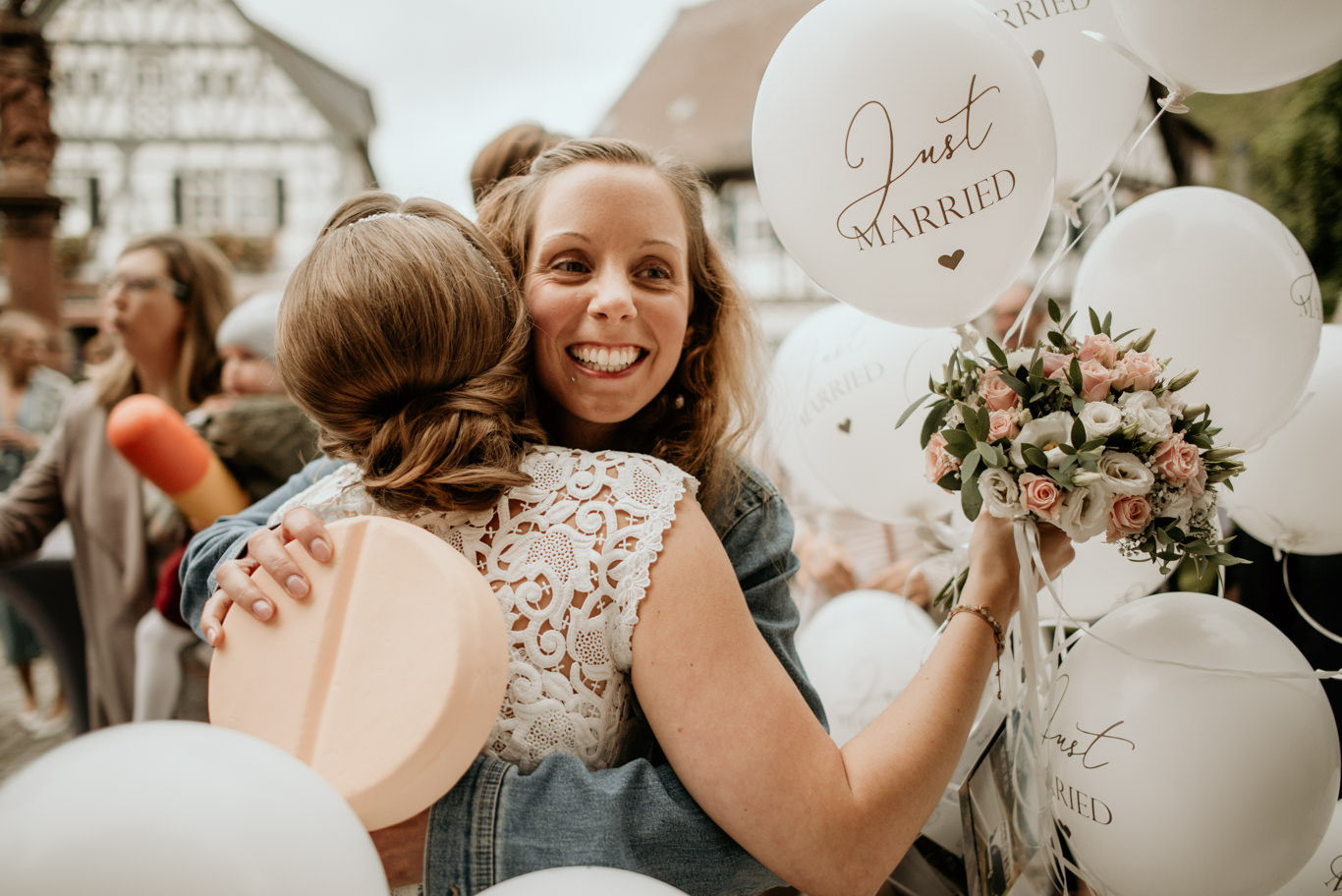 Braut umarmt lachend eine Freundin, im Hintergrund weiße Luftballons
