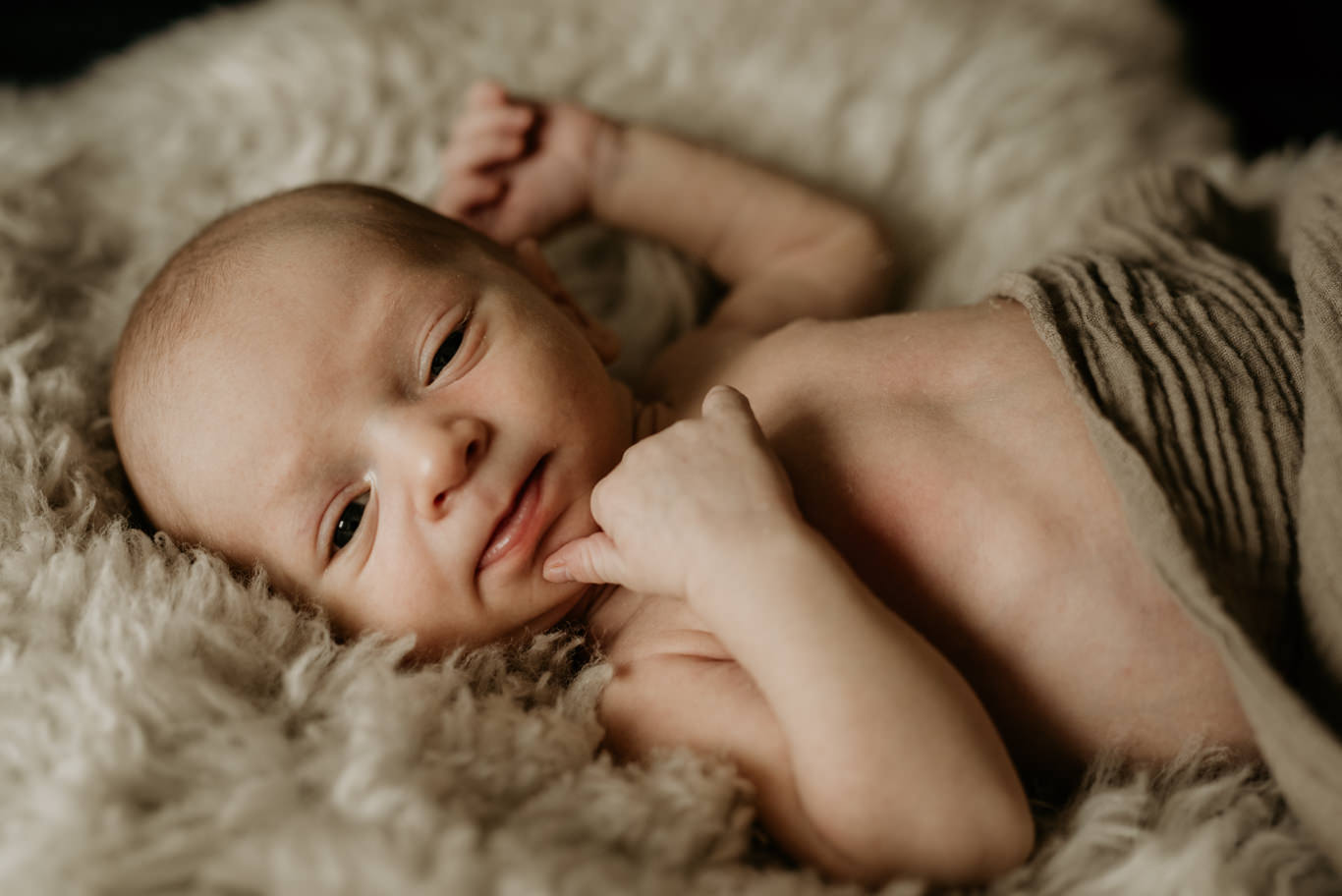 Baby liegt unbekleidet auf Fell und blickt in die Kamera