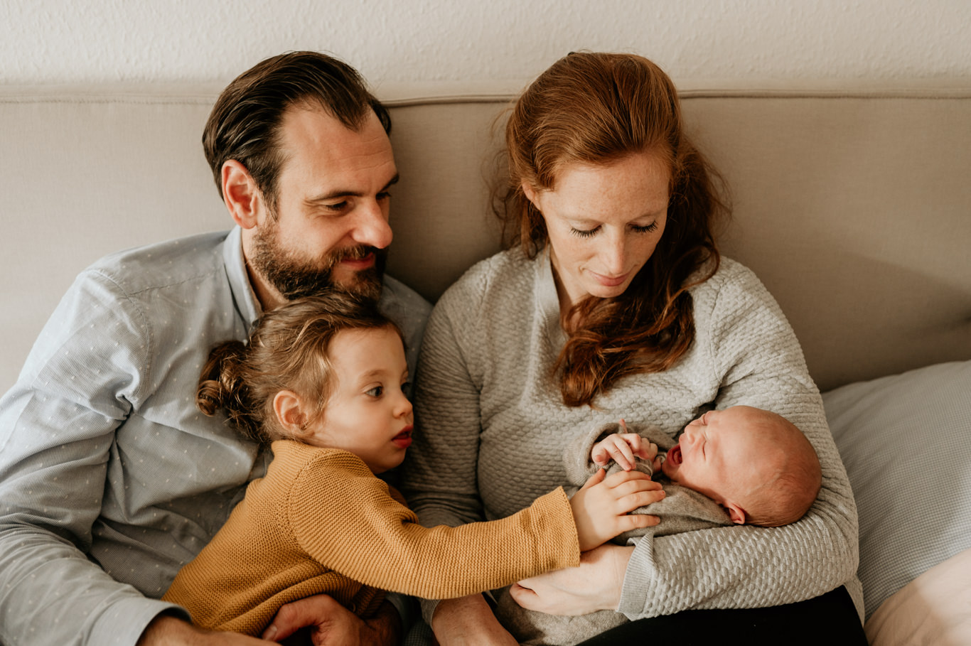 Eltern sitzen mit Kleinkind, das behutsam das Baby berührt