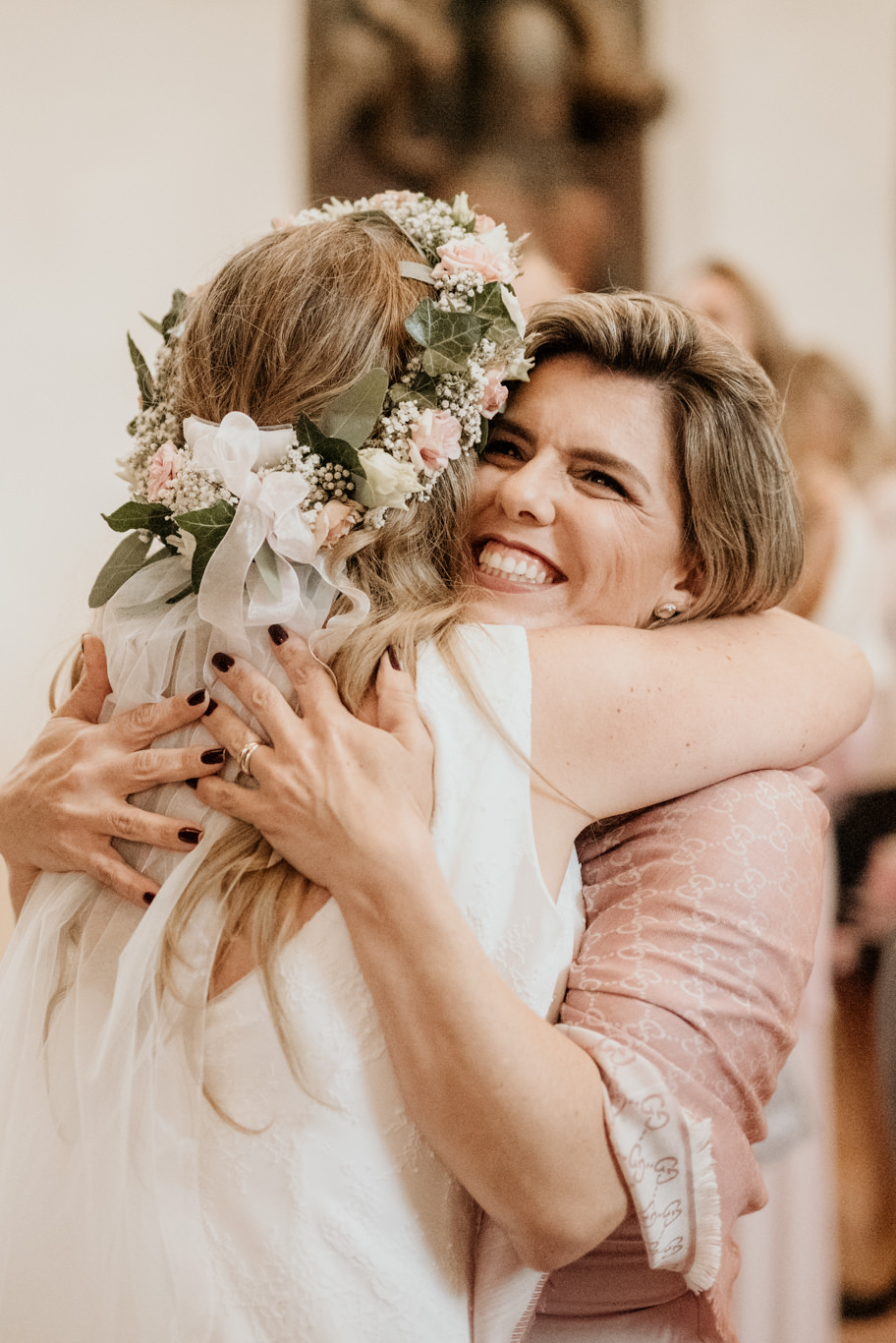 Braut mit Blumenkranz umarmt lachend eine Gästin