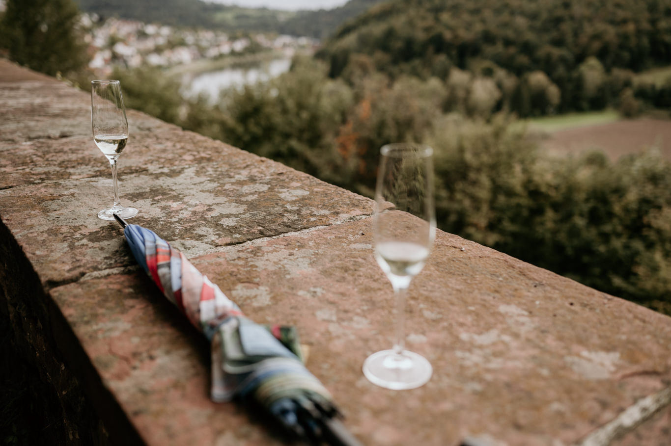 Zwei Sektgläser stehen auf einer Steinmauer mit Ausblick über das Tal
