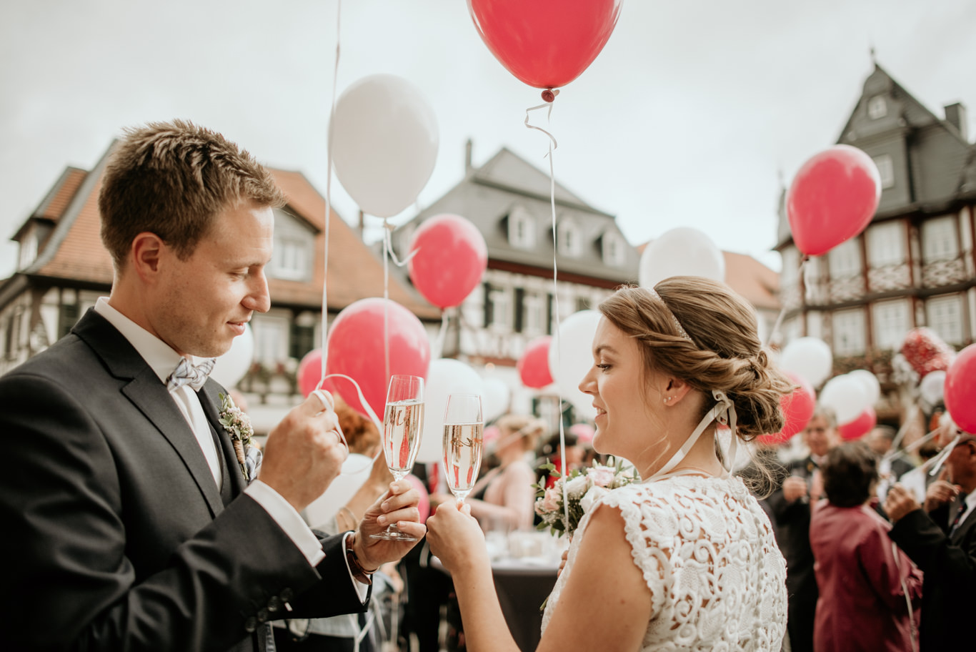 Bräutigam und Braut stoßen mit Sektgläsern zwischen bunten Luftballons an