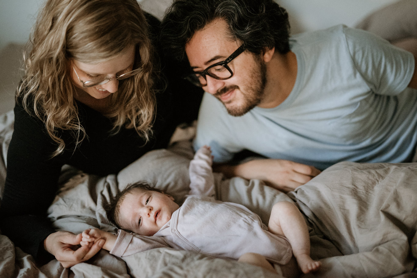 Eltern beugen sich lächelnd über ihr schlafendes Baby im Bett