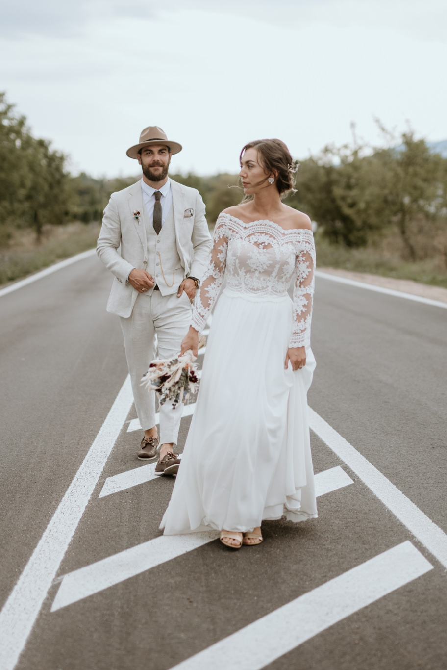 Boho-Brautpaar geht Hand in Hand über eine Straße