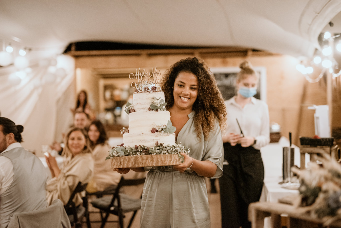 Braut trägt lachend eine mehrstöckige Hochzeitstorte zum Tisch