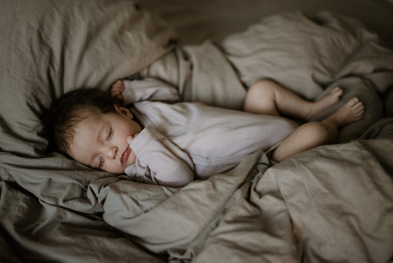 Baby schläft ausgestreckt auf dem Bett in weichem Licht
