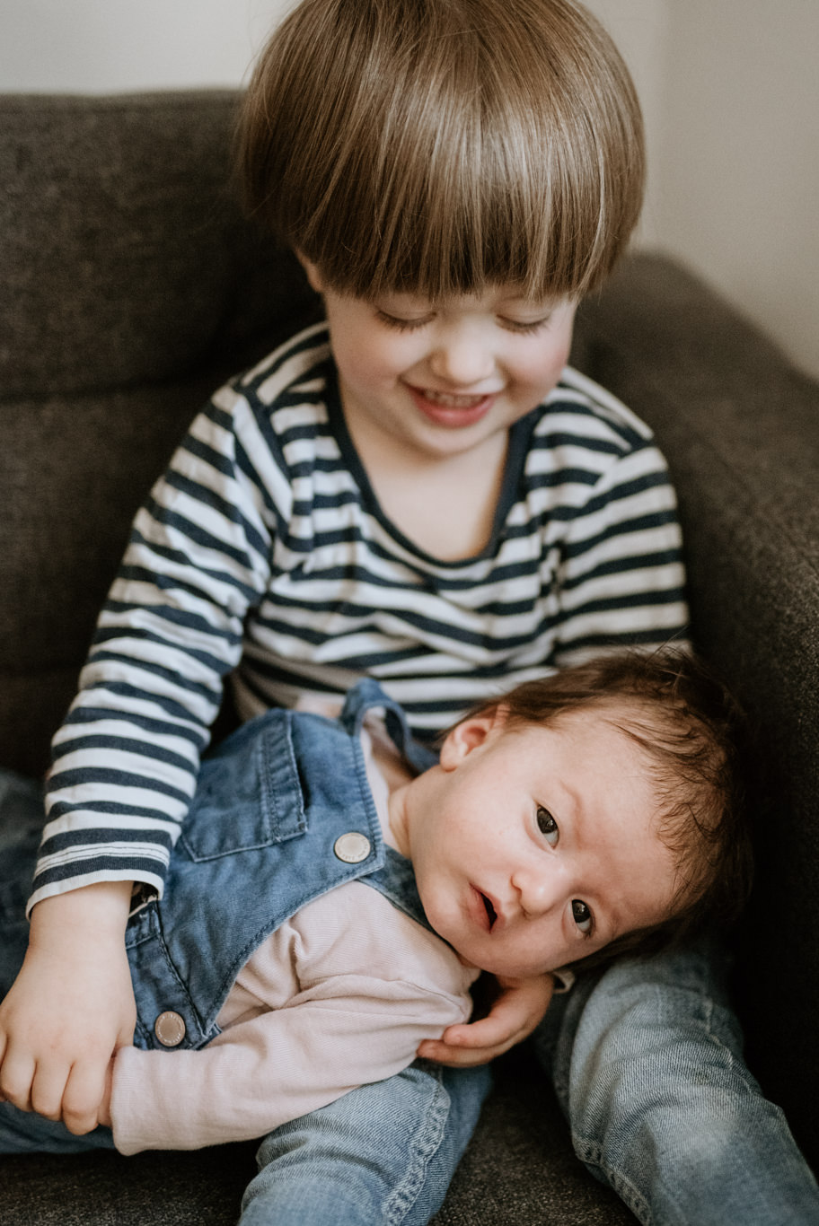 Junge hält lächelnd sein Baby-Geschwisterchen auf dem Schoß