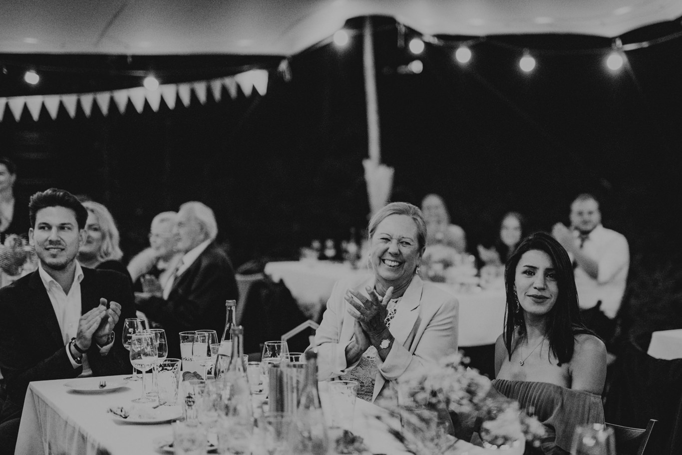 Schwarzweißaufnahme applaudierender Gäste an der festlich gedeckten Tafel