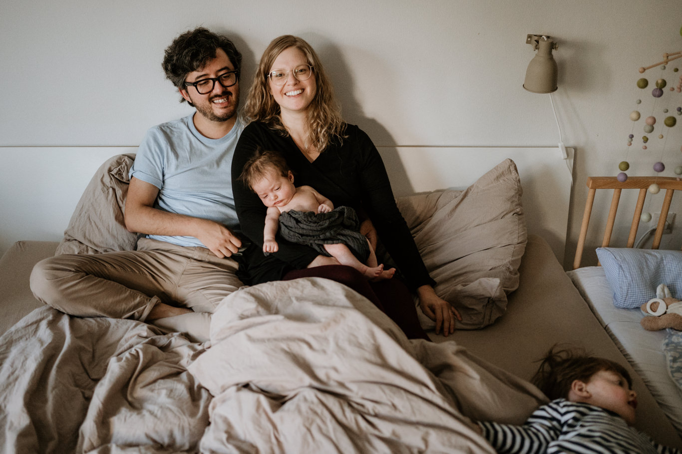 Familie sitzt lachend mit Baby und Kind auf dem Bett
