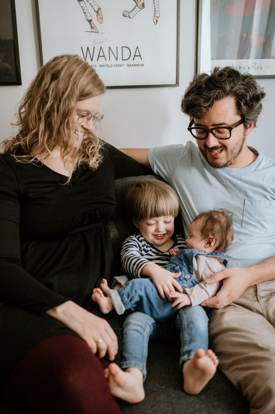 Eltern sitzen mit ihren beiden Kindern lachend eng zusammen auf dem Sofa