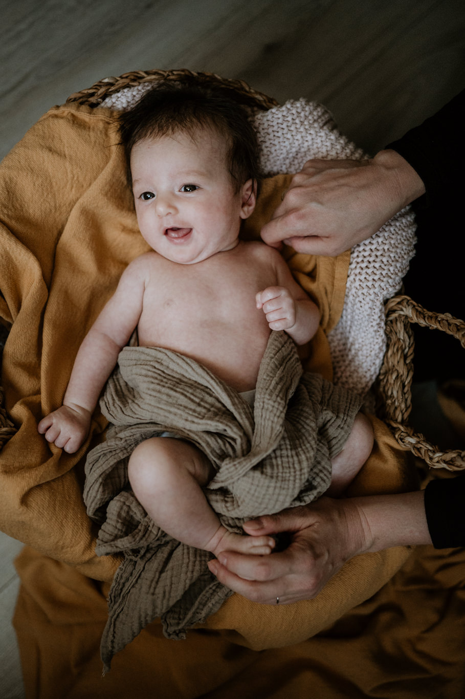 Baby liegt lachend in gestreiftem Tuch im Korb