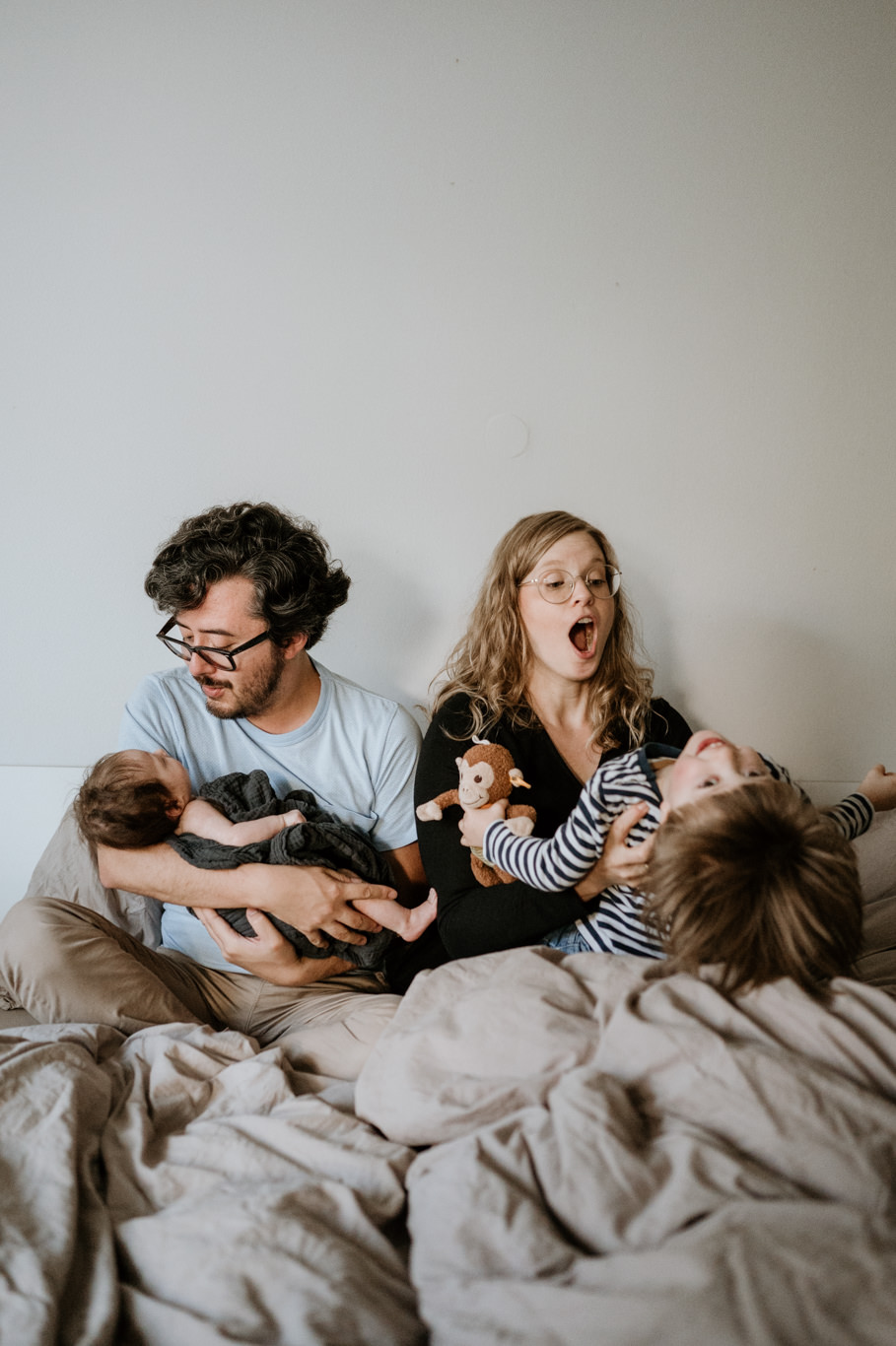 Vater hält lachend Baby, Kind lacht daneben auf dem Bett