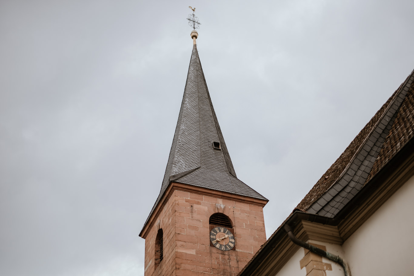 Kirchturm ragt vor bewölktem Himmel in Deidesheim auf