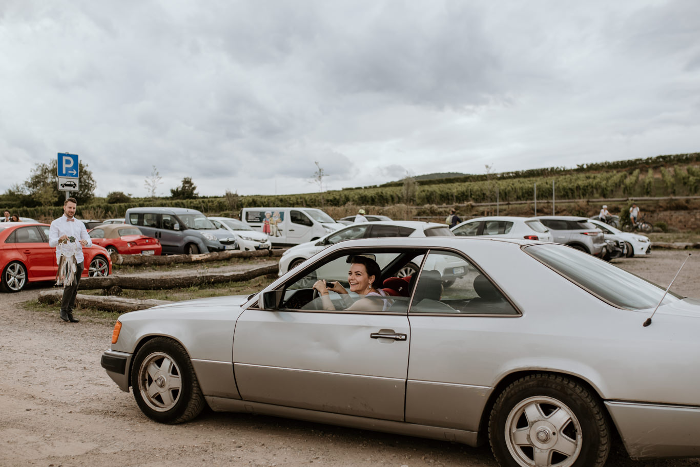 Brautpaar sitzt lächelnd in einem Oldtimer auf dem Parkplatz