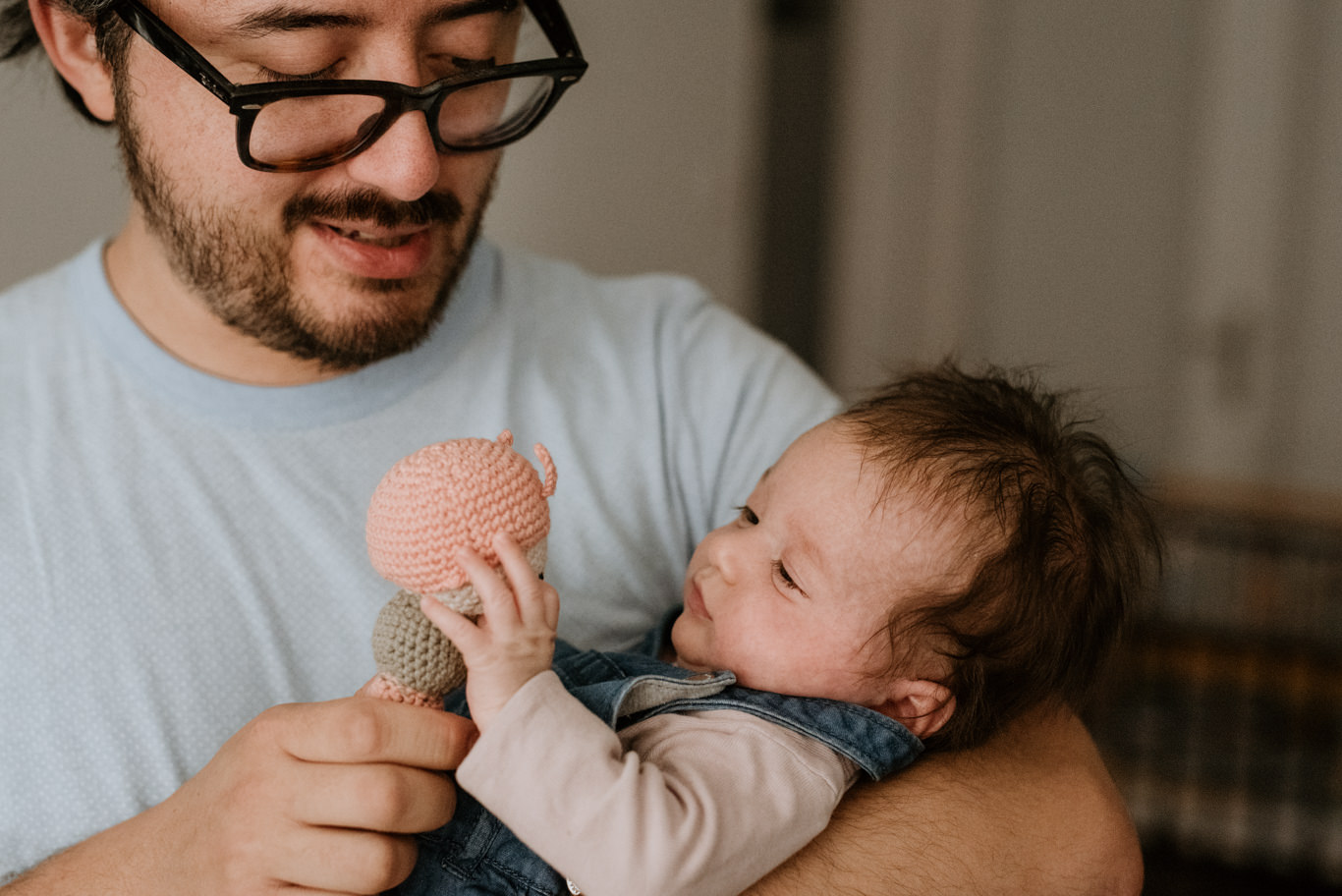 Vater lächelt sein Baby an und hält ein Rasselspielzeug