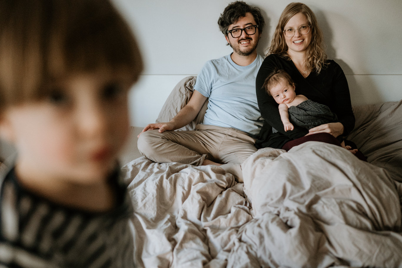 Kind sitzt vorne auf dem Bett, Familie im Hintergrund