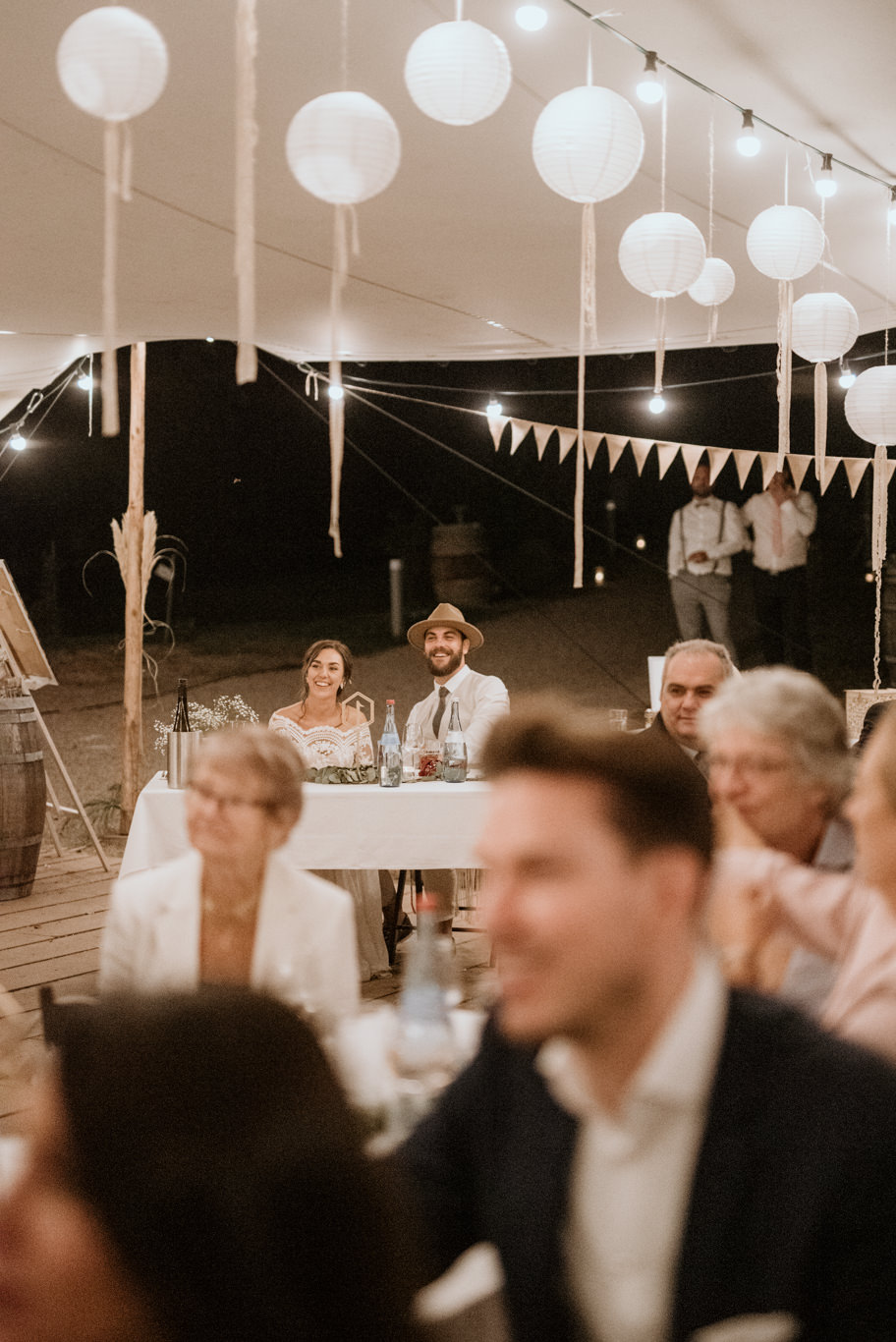Gäste sitzen an der Tafel unter Lampions im Festzelt