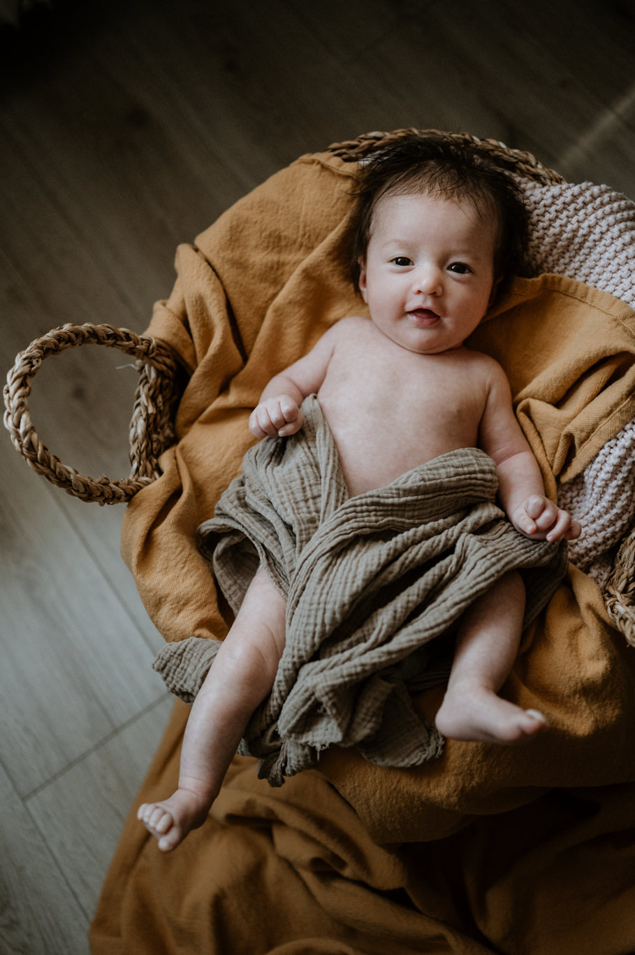 Baby liegt lächelnd in einem Weidenkorb mit Wolldecke