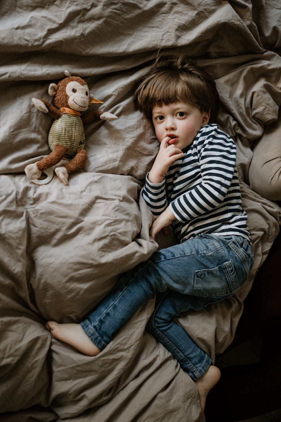 Kind liegt mit Stofftier auf dem Bett und blickt zur Seite