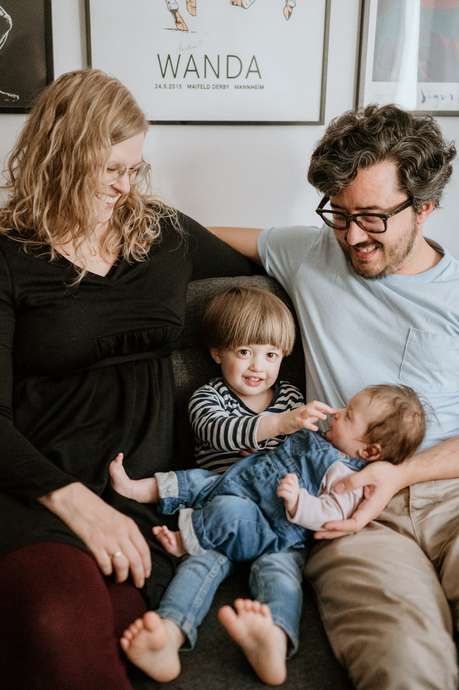 Eltern beugen sich lächelnd über ihr Neugeborenes, der Sohn schaut zu
