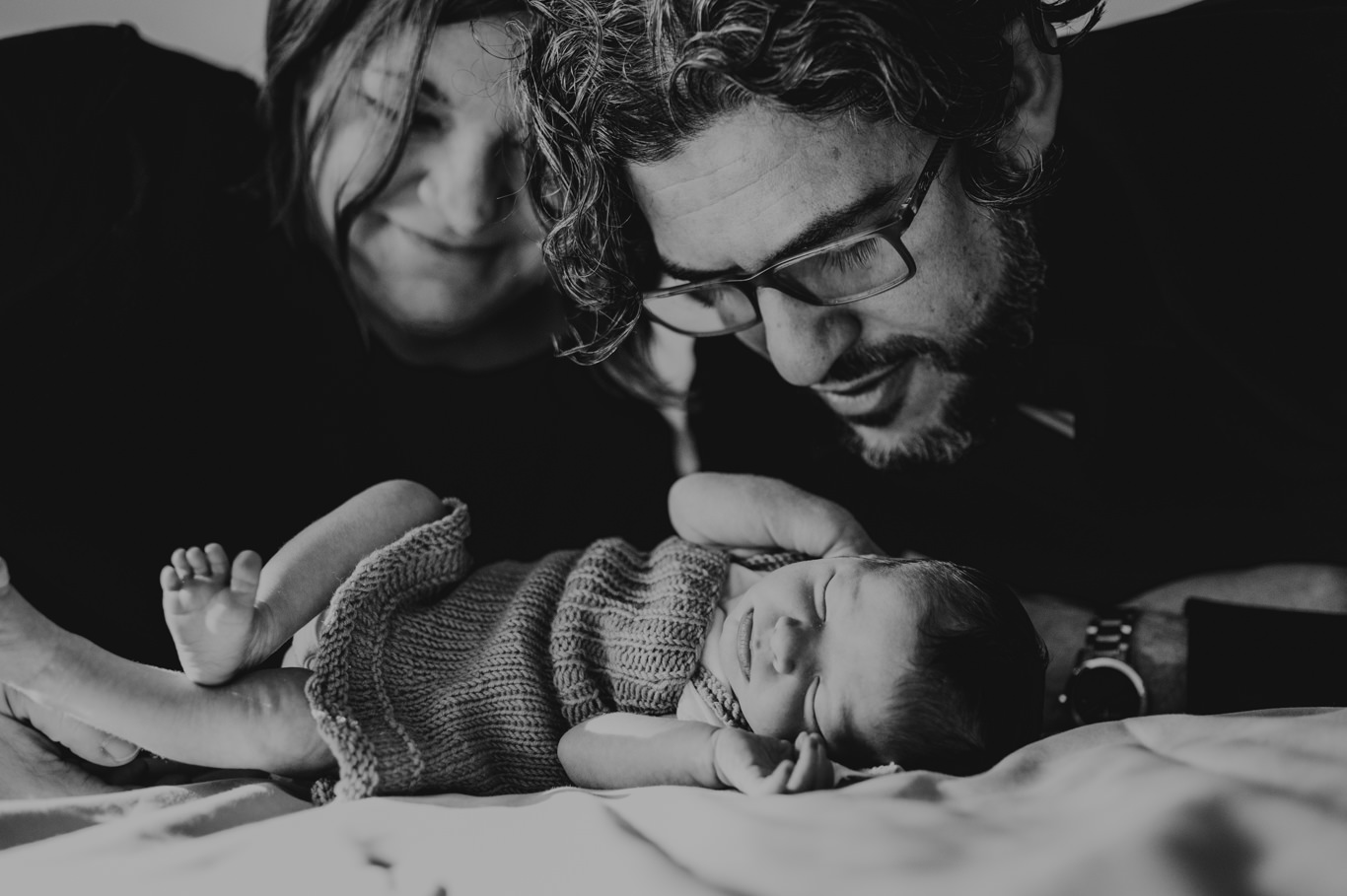 Eltern betrachten liebevoll ihr schlafendes Baby, Schwarzweißaufnahme