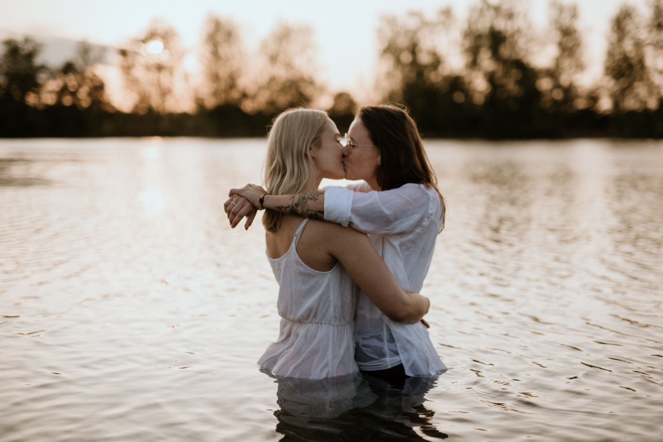 Zwei Frauen küssen sich stehend im See im Gegenlicht