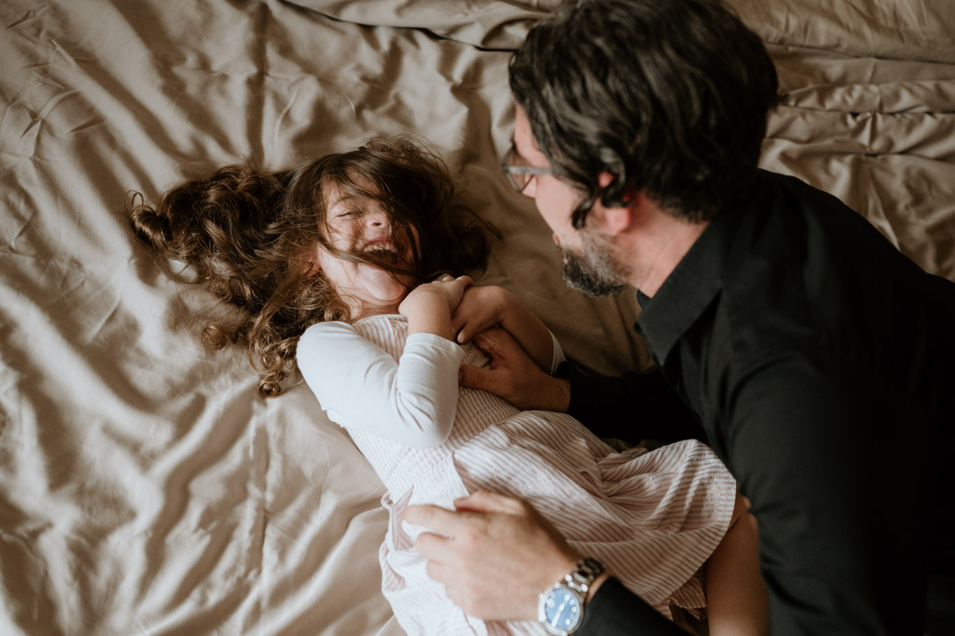 Vater kitzelt lachend seine Tochter auf dem Bett