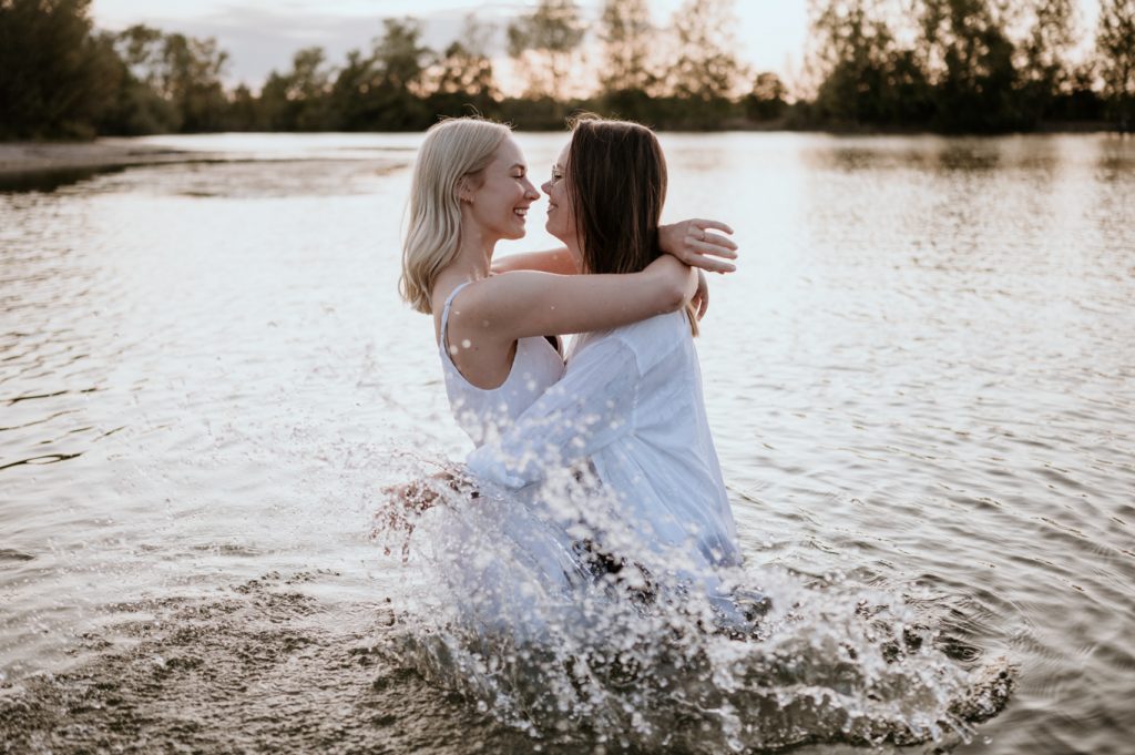 Zwei Frauen in weißen Kleidern umarmen sich lachend im Wasser bei Ludwigshafen