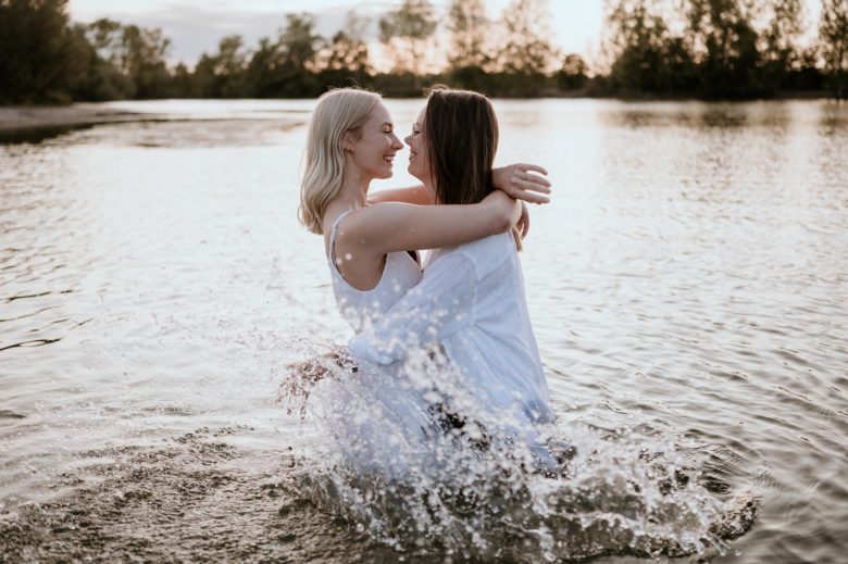 Zwei Frauen in weißen Kleidern umarmen sich lachend im Wasser bei Ludwigshafen