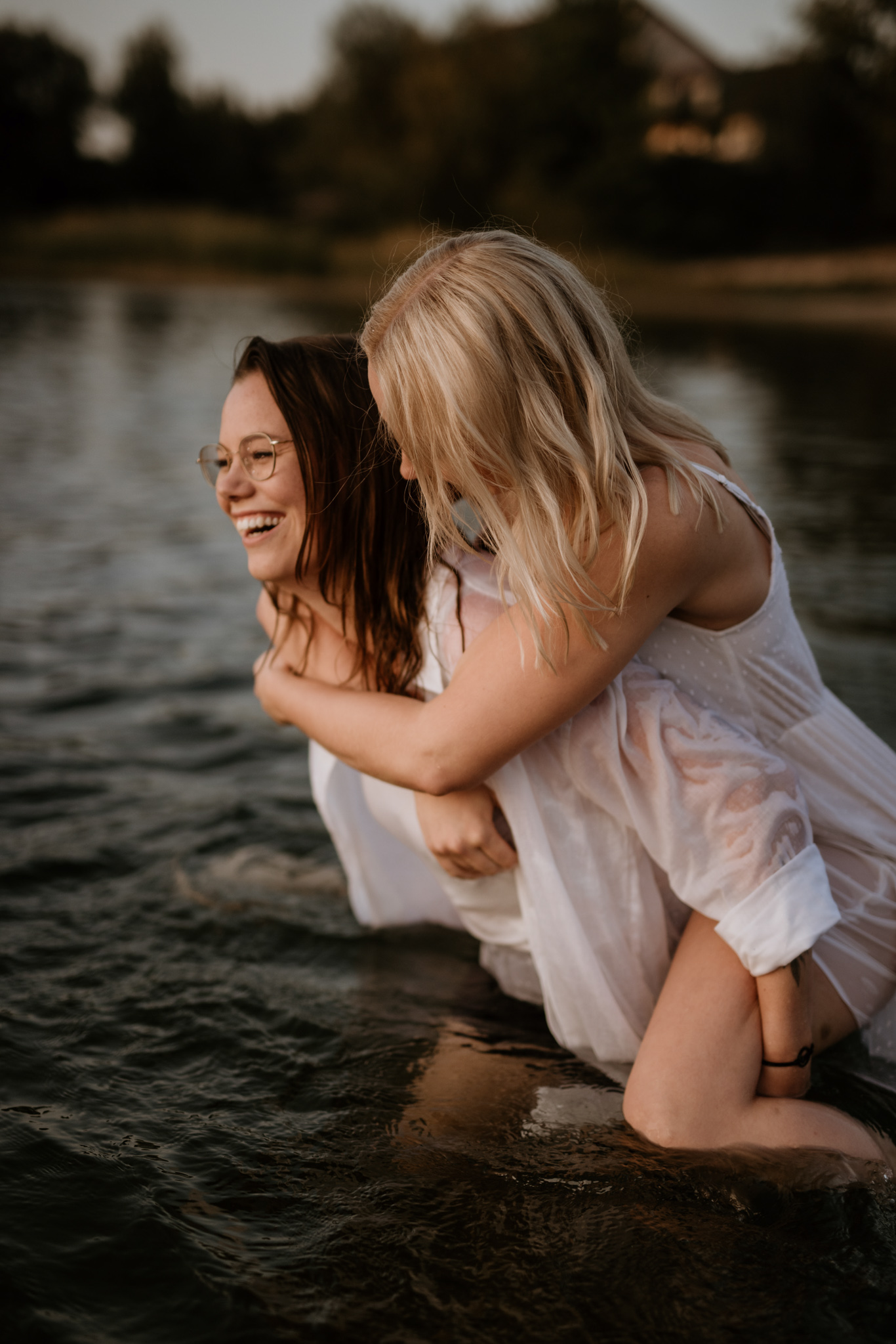 Zwei Frauen tragen sich lachend huckepack durch das seichte Wasser