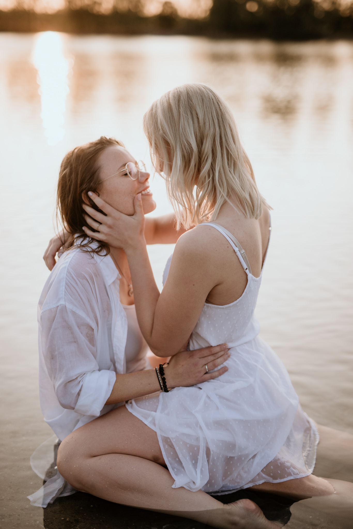 Zwei Frauen sitzen im Sonnenuntergang eng aneinander am See