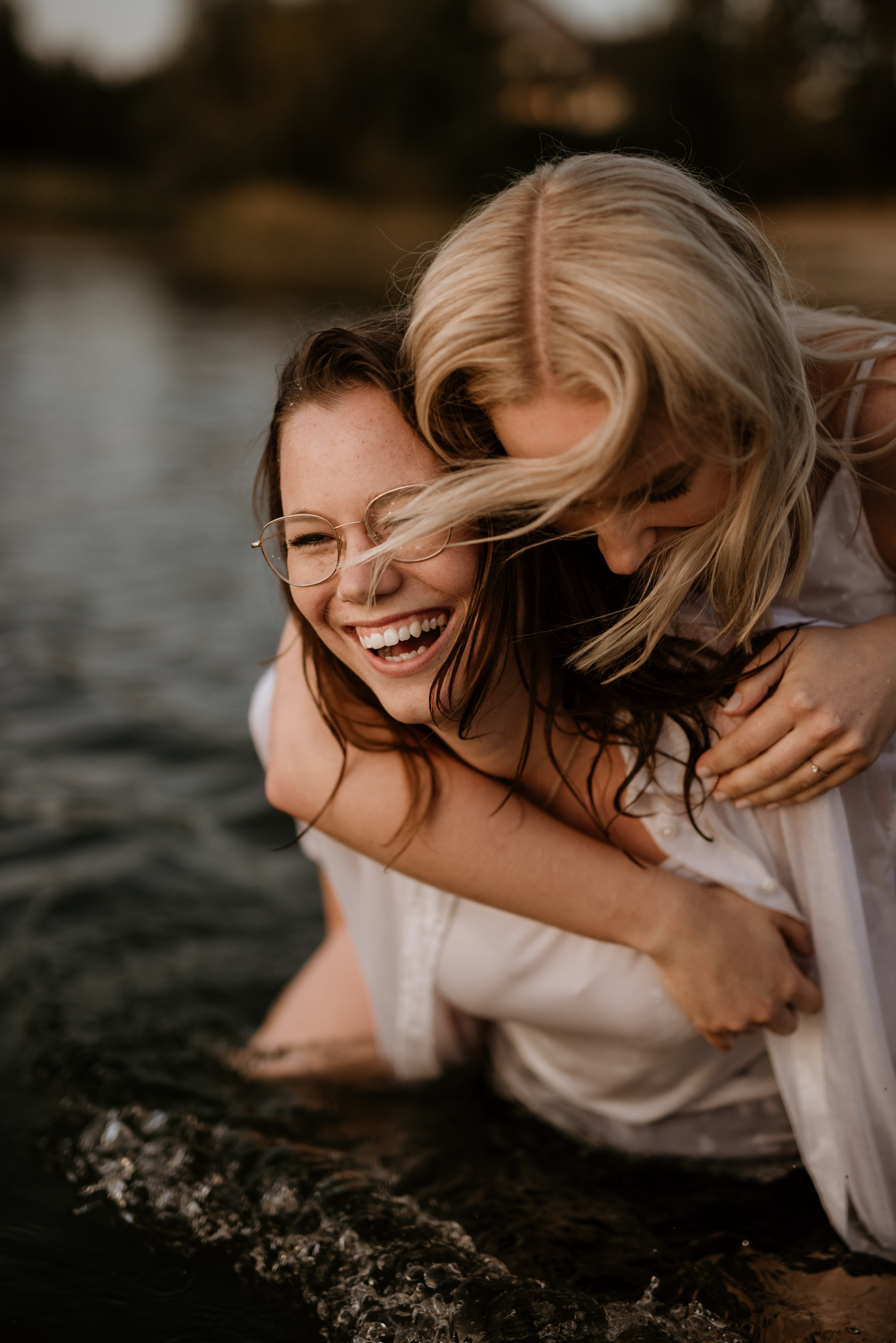 Zwei Frauen lachen kniend im flachen Wasser am Ufer