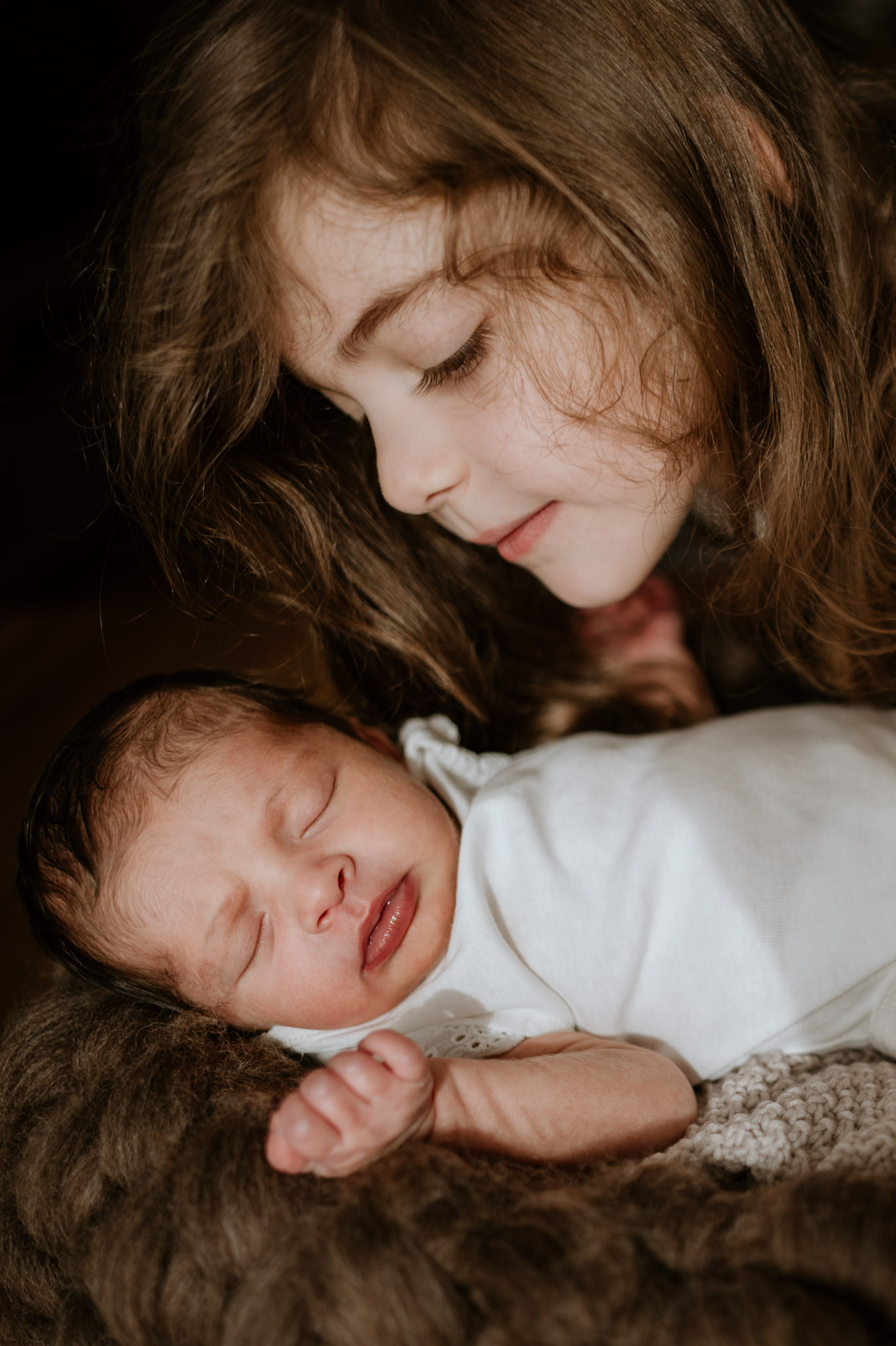 Mädchen kuschelt seine Wange sanft an das schlafende Baby